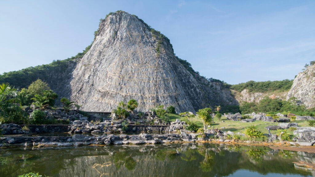 Golden Buddha engraving on Khao Chi Chan limestone cliff reflected in the pond in Pattaya, Thailand