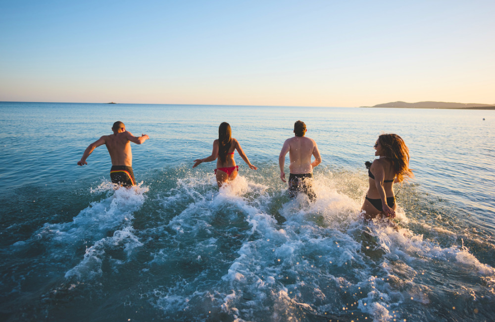 A group of friends running into the sea during sunset at a Pattaya beach, capturing the joy and energy of a tropical getaway near Altera Hotel and Residence.