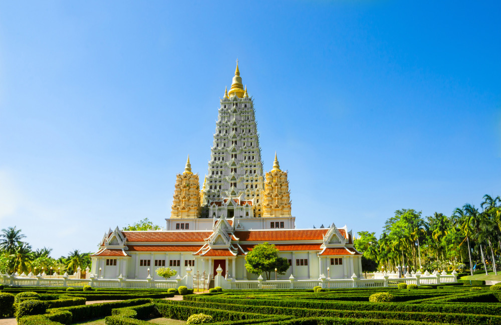 Front view of Wat Yansangwararam in Pattaya, featuring its distinctive white and gold prang structure surrounded by manicured gardens and peaceful blue skies—an elegant cultural site near Altera Hotel and Residence.