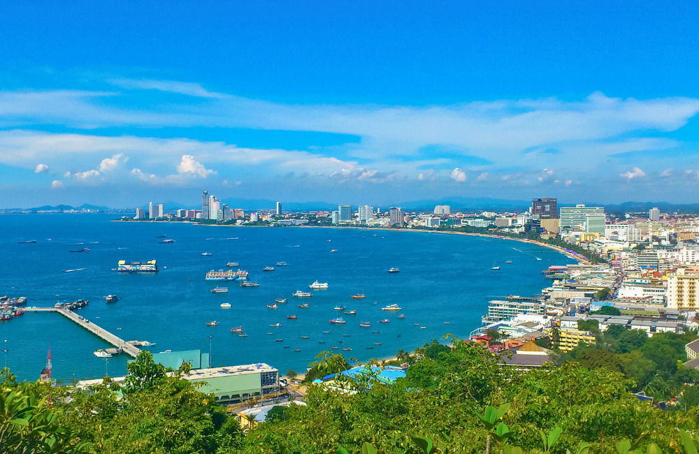 A scenic aerial view of Pattaya Bay with boats, high-rise buildings, and a long stretch of beach, seen from Khao Phra Tamnak near Altera Hotel and Residence.