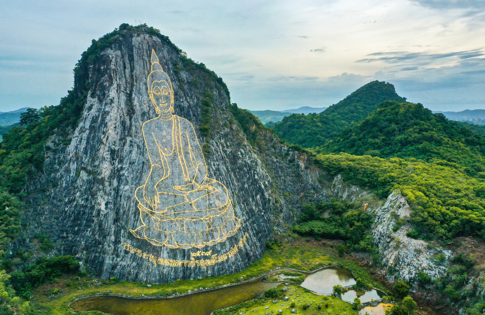 The giant golden Buddha image engraved on Khao Chi Chan cliff, a peaceful cultural and natural attraction near Pattaya surrounded by lush greenery and mountain views.