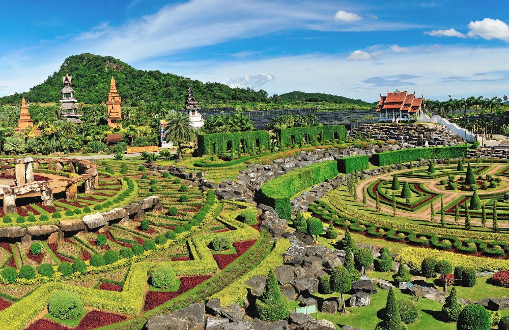A vibrant aerial view of Nong Nooch Tropical Garden in Pattaya, featuring landscaped gardens, Thai architecture, and mountain backdrops—an ideal family attraction near Altera Hotel and Residence.