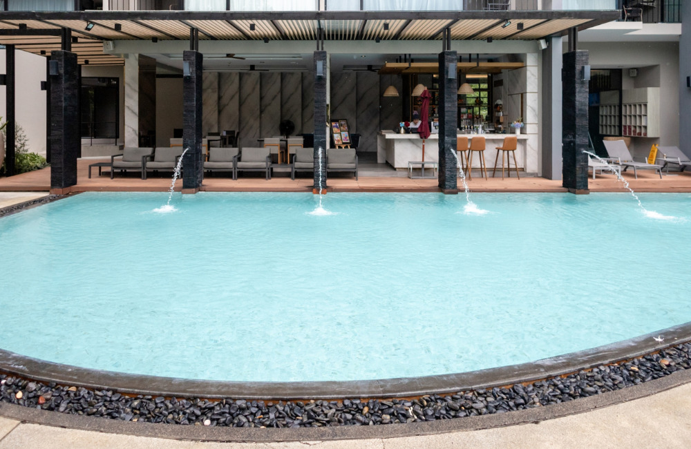 The expansive outdoor swimming pool at Altera Hotel & Residence Pattaya with red umbrellas and sun loungers, offering the best daily rates for direct bookings.