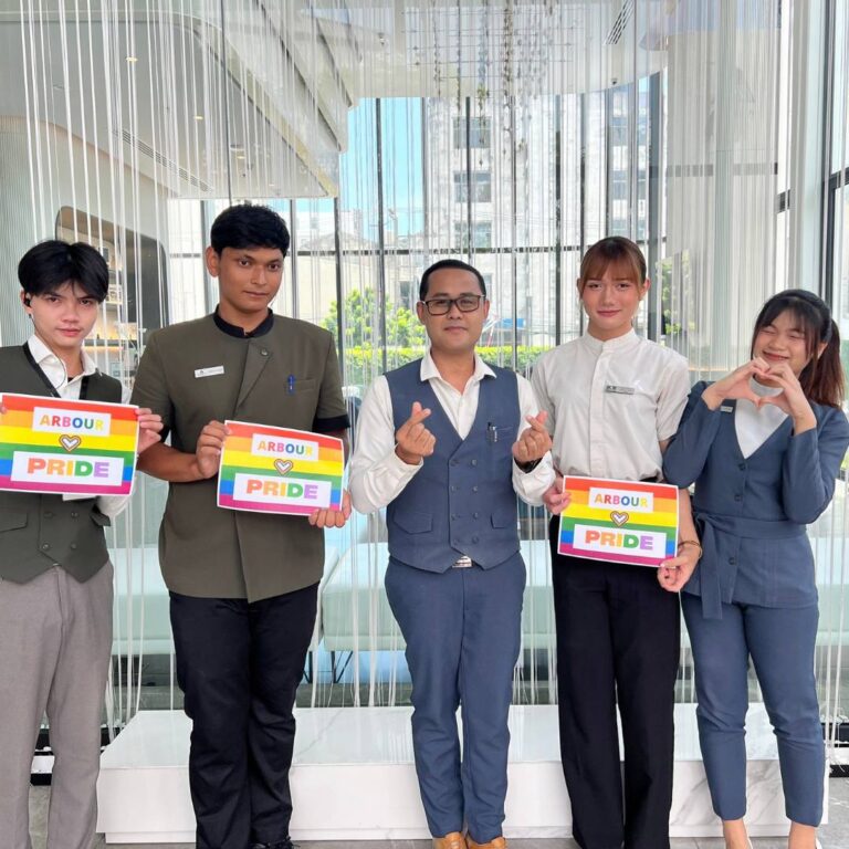 A group of five staff members at Arbour Hotel and Residence Pattaya, dressed in professional uniforms, smiling and holding Pride-themed signs that read “ARBOUR ❤️ PRIDE.” They are making heart hand gestures, showcasing their support for diversity and inclusion.