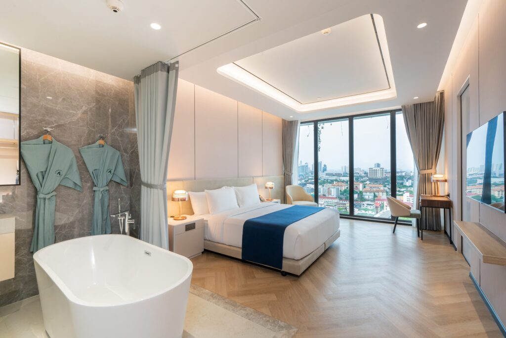 Luxurious hotel room featuring a spacious layout with a freestanding bathtub, king-sized bed, panoramic city view, and elegant modern decor.