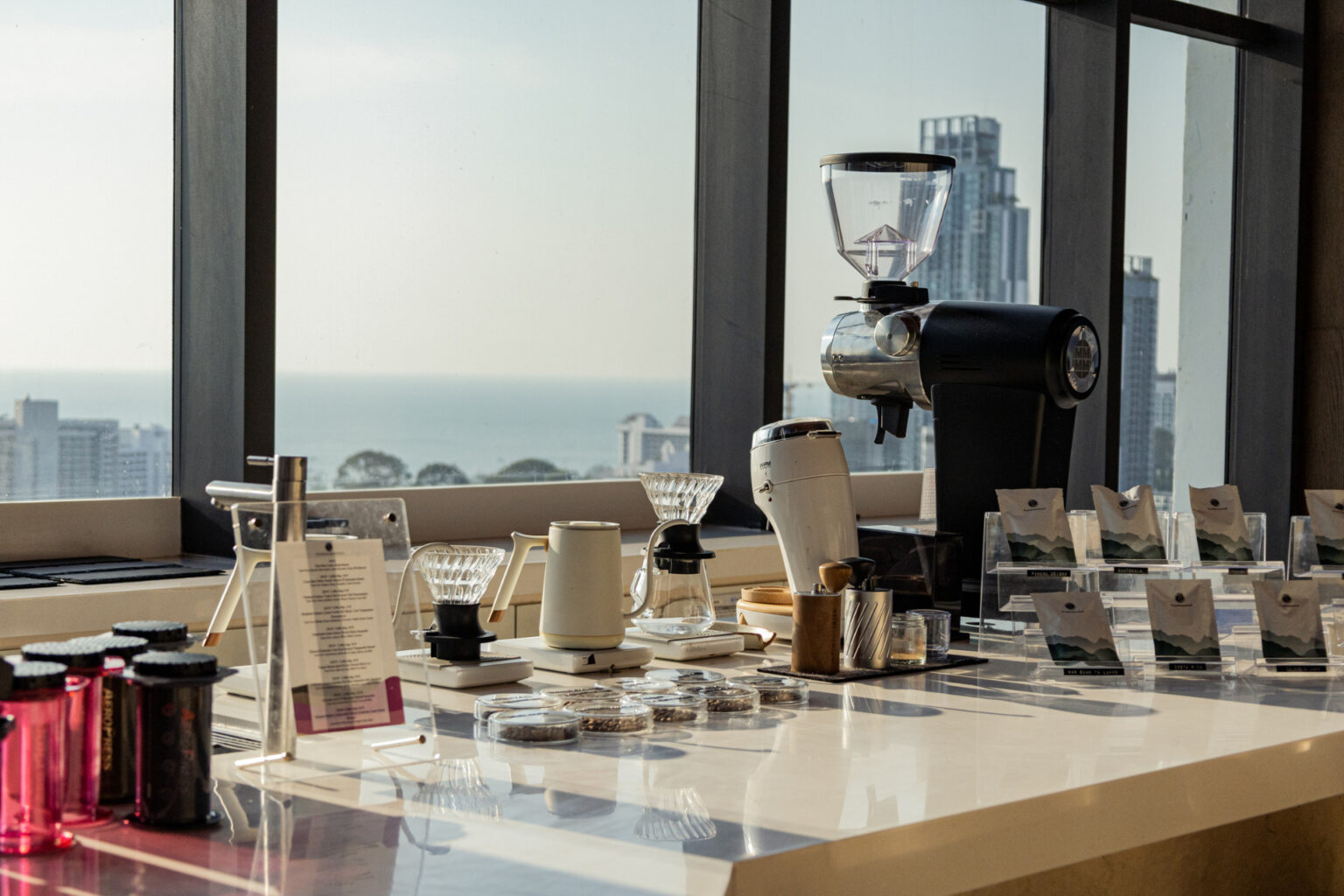 A modern coffee brewing station set against a panoramic view of Pattaya city and the ocean, showcasing premium coffee-making equipment and neatly arranged coffee beans.