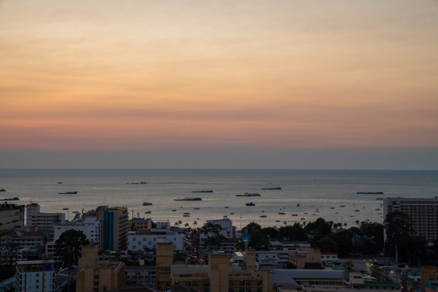 Panoramic view of Pattaya city and the ocean at dusk with vibrant orange and pink hues in the sky.