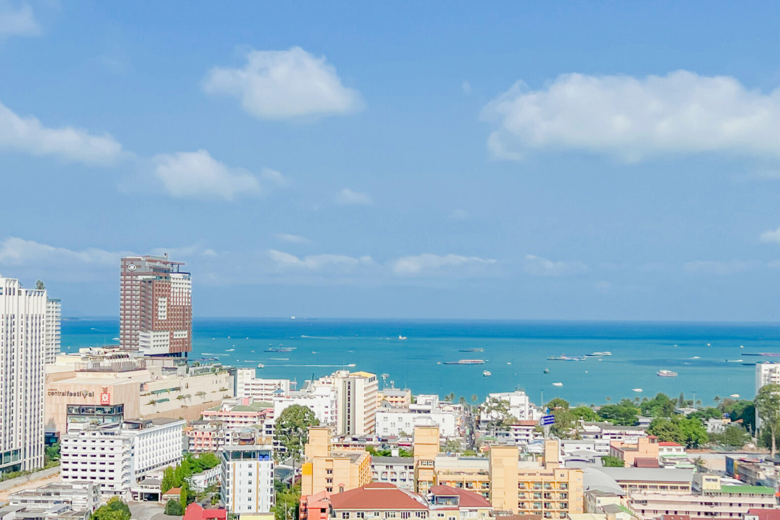 Stunning daytime view of Pattaya city with buildings and the turquoise ocean under a bright blue sky.