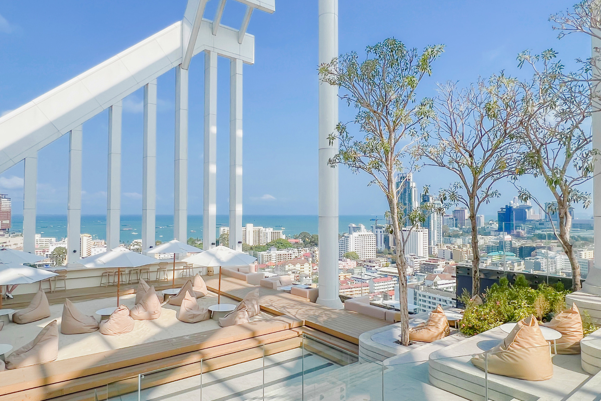 Elegant rooftop bar at Arbour Hotel and Residence Pattaya with bean bag seating, white umbrellas, and panoramic city and ocean views.