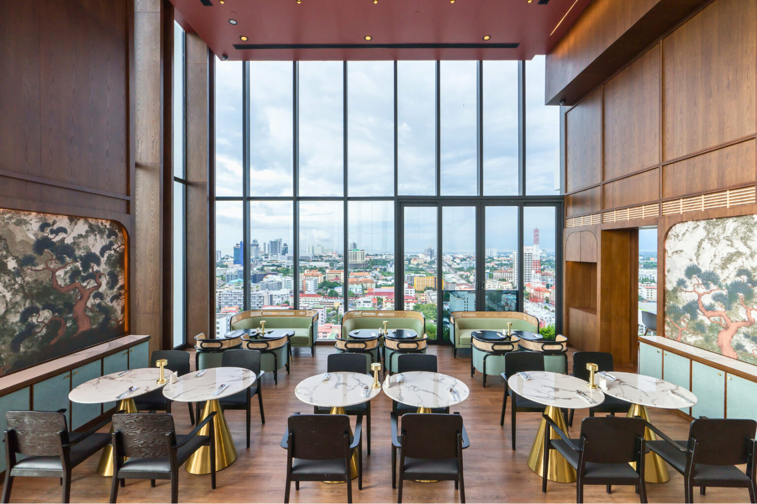 Elegant dining area with floor-to-ceiling windows offering panoramic views of Pattaya city, featuring marble tables and luxurious decor.