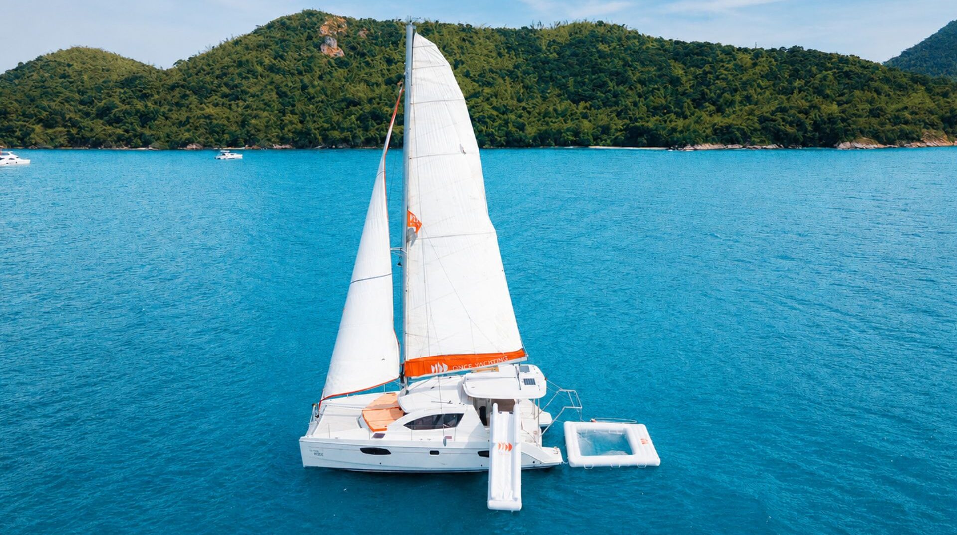 White sailing catamaran with water platforms floating on clear blue sea near a green tropical island during a Pattaya yacht experience.