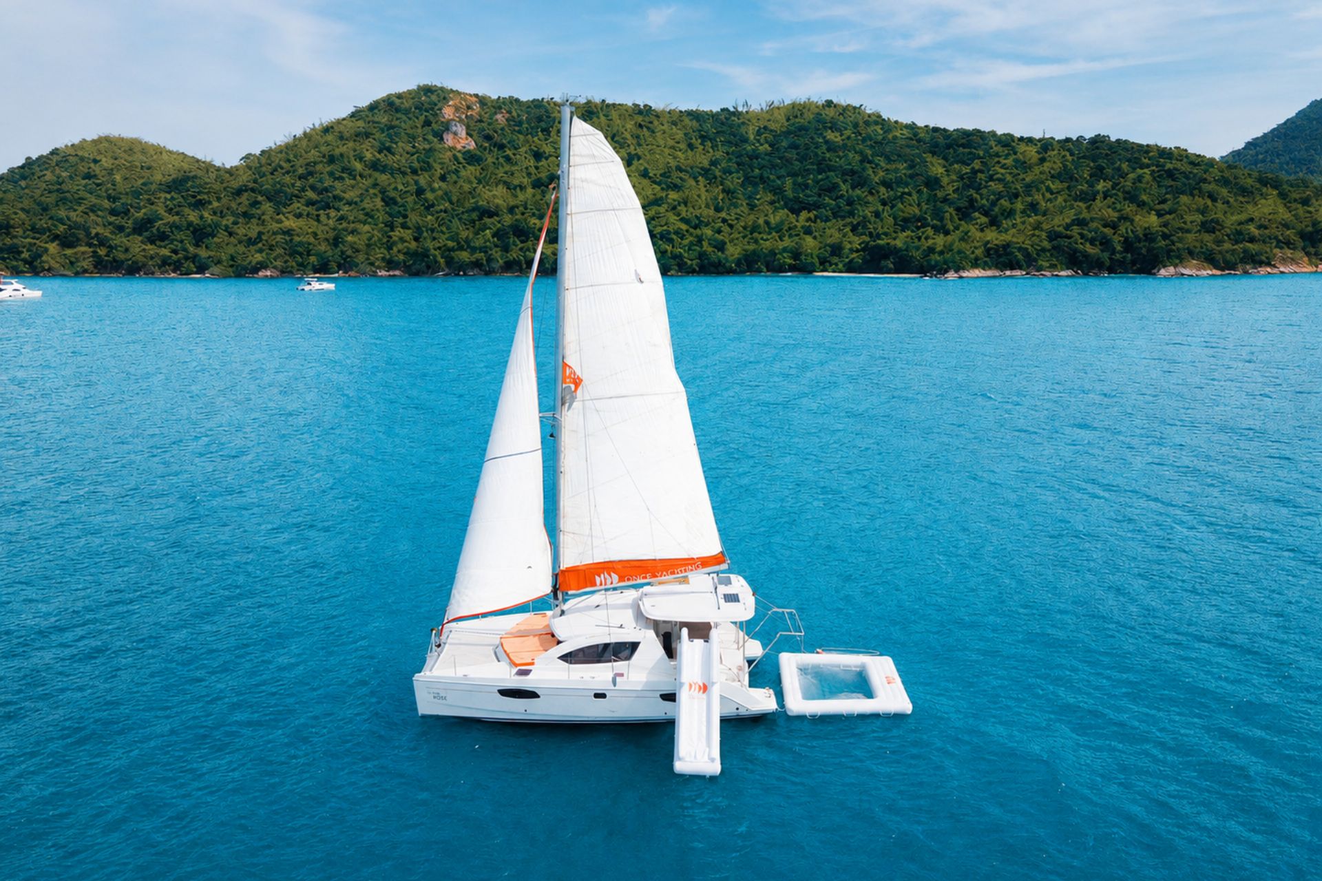 White sailing catamaran with water platforms floating on clear blue sea near a green tropical island during a Pattaya yacht experience.