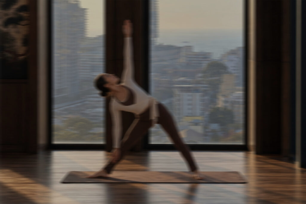 Woman practicing a Pilates side stretch on a mat beside floor-to-ceiling windows overlooking Pattaya, creating a calm wellness setting for Pilates in Paint.