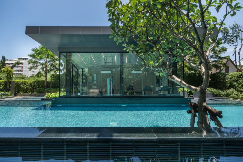 Outdoor swimming pool at Arden Hotel and Residence Pattaya with a modern glass-walled fitness center surrounded by tropical greenery.