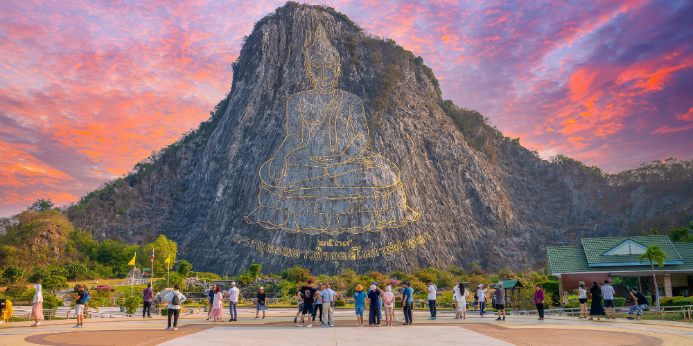 นักท่องเที่ยวเยี่ยมชมพระพุทธรูปแกะสลักเลเซอร์บนหน้าผาหินปูนที่เขาชีจรรย์ พัทยา จุดแลนด์มาร์กสำคัญใกล้ไร่องุ่นซิลเวอร์เลคและสวนน้ำรามายณะ