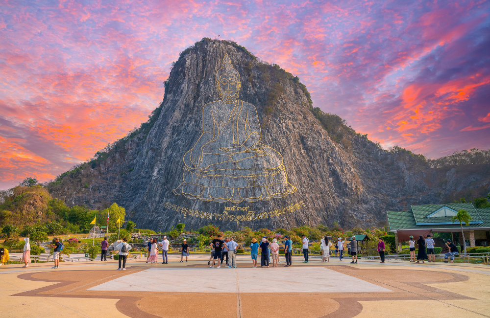 นักท่องเที่ยวเยี่ยมชมพระพุทธรูปแกะสลักเลเซอร์บนหน้าผาหินปูนที่เขาชีจรรย์ พัทยา จุดแลนด์มาร์กสำคัญใกล้ไร่องุ่นซิลเวอร์เลคและสวนน้ำรามายณะ