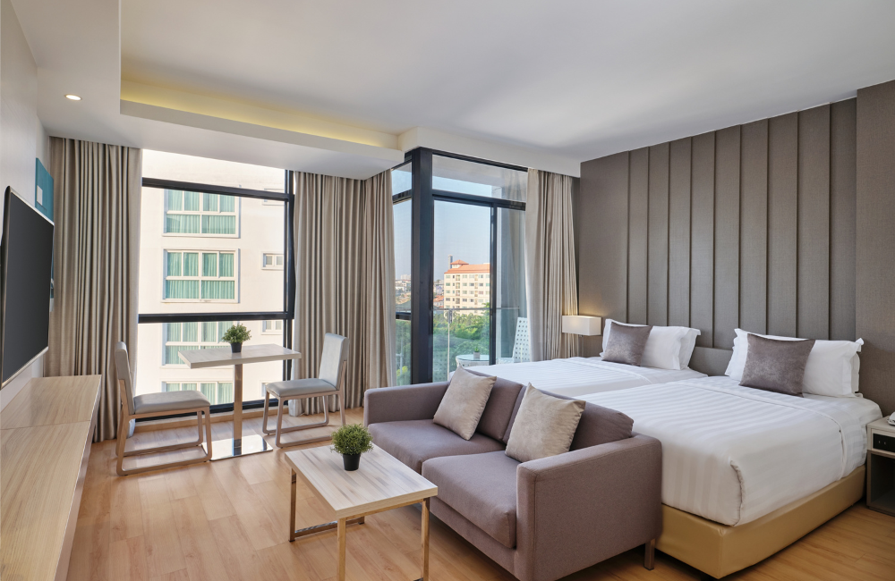 Bright Deluxe Room at Arden Hotel Pattaya with twin beds, dining space, sofa, and large windows with city view.