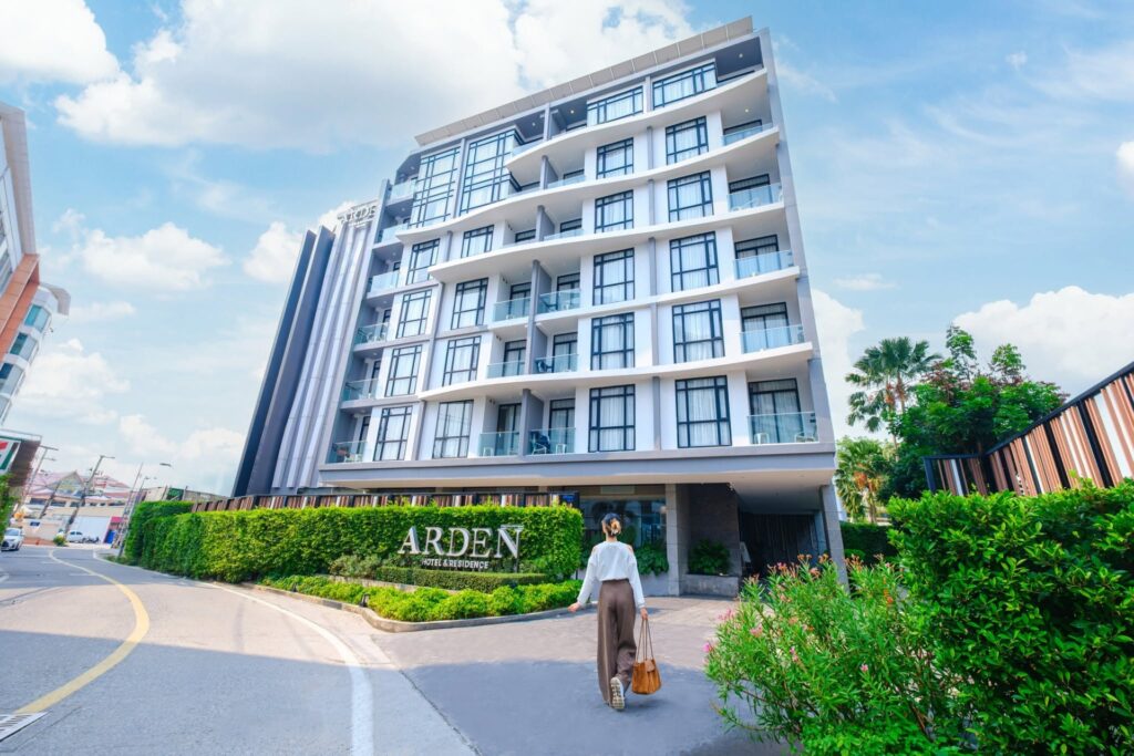 Guest walking toward the entrance of Arden Hotel and Residence Pattaya, featuring a modern white façade, glass balconies, and landscaped greenery.