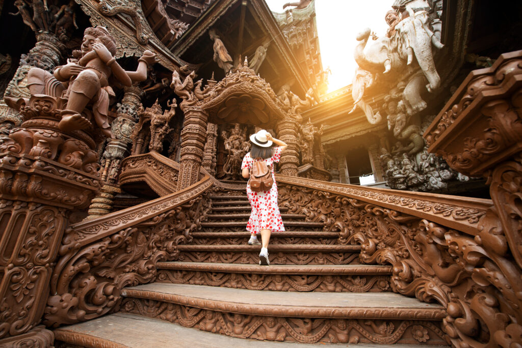 Traveler walking up the ornate steps of the Sanctuary of Truth, a stunning wooden temple near Hotel Amber Pattaya, a top Pattaya hotel located close to this iconic attraction.