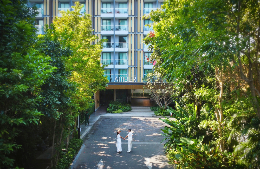Couple enjoying a romantic weekend getaway in front of Hotel Amber Pattaya entrance surrounded by lush greenery.