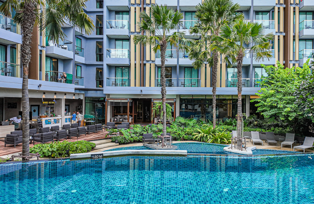 Outdoor swimming pool surrounded by palm trees at Hotel Amber Pattaya, perfect for a relaxing weekend getaway near Soi Buakhao.