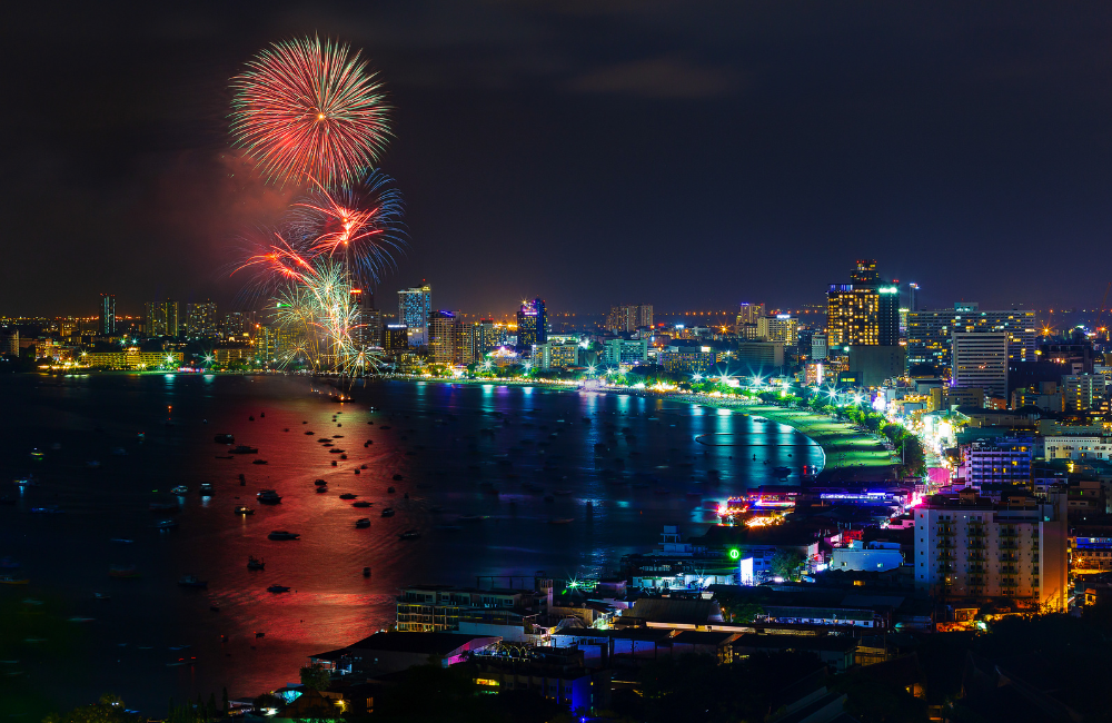 Spectacular fireworks display lighting up Pattaya Bay during the New Year countdown celebration with city lights reflecting on the water.