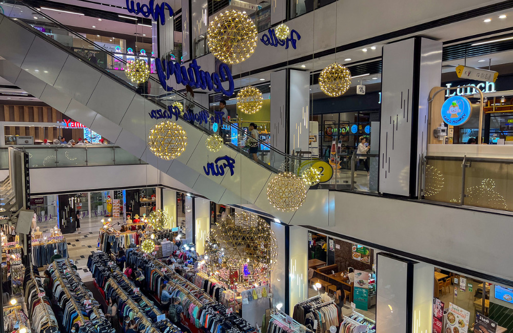 Interior of a vibrant shopping mall with escalators, decorative lighting, clothing stalls, and restaurants at Century The Movie Plaza Sukhumvit.