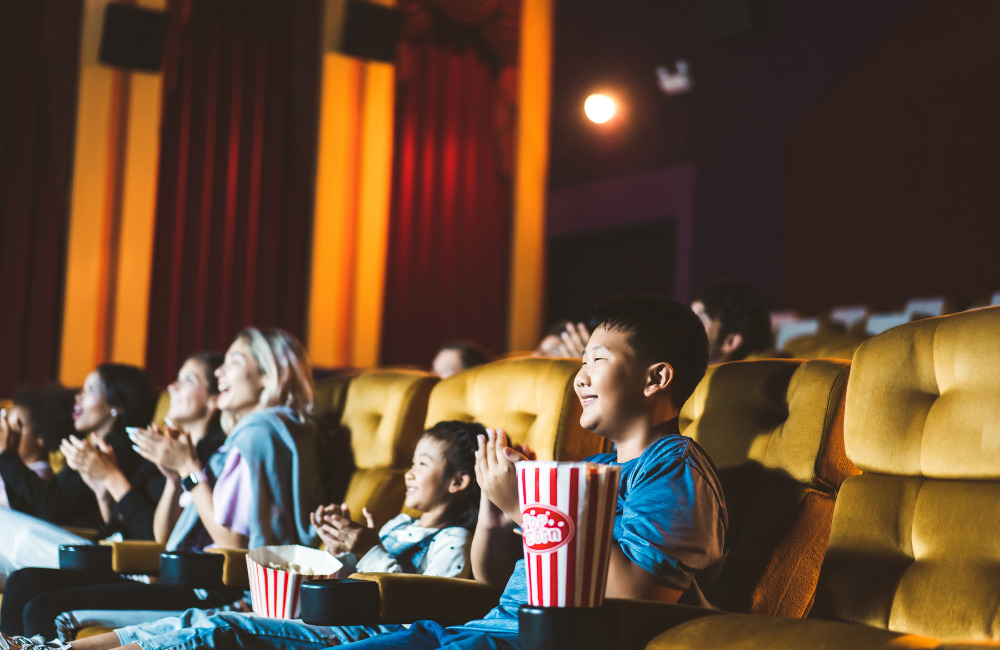 A family enjoying a movie at Century The Movie Plaza Sukhumvit, sitting in comfortable yellow seats with popcorn and smiles.