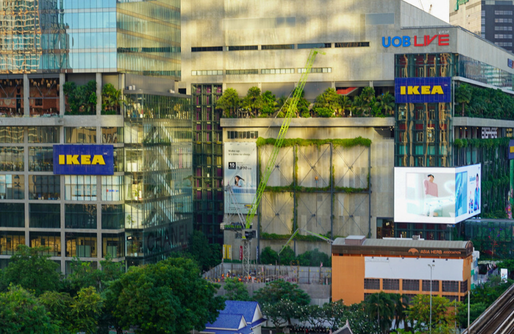 Aerial view of EmSphere in Bangkok, highlighting the UOB Live Arena, IKEA's city store, and lush vertical gardens on the building's façade. The scene includes modern architecture and branded displays.