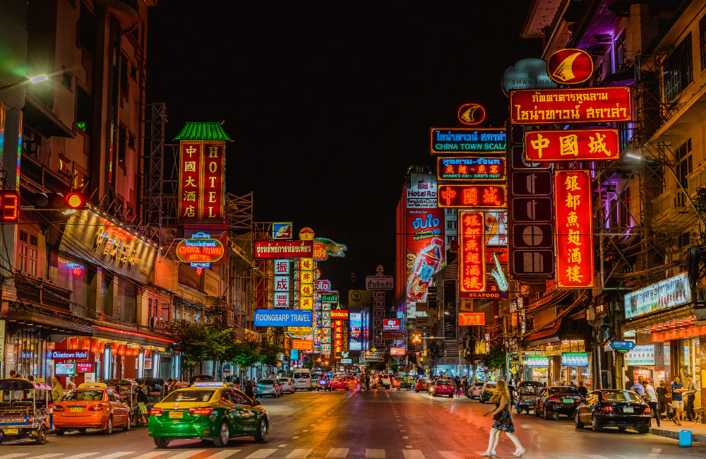 Night view of Bangkok Chinatown’s Yaowarat Road filled with neon signs, cars, and pedestrians under a vibrant street scene.