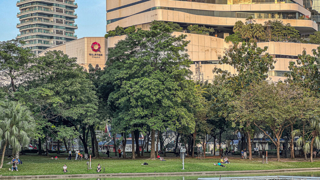 Trees and open lawn at Benjasiri Park Bangkok with Quartier CineArt in the background