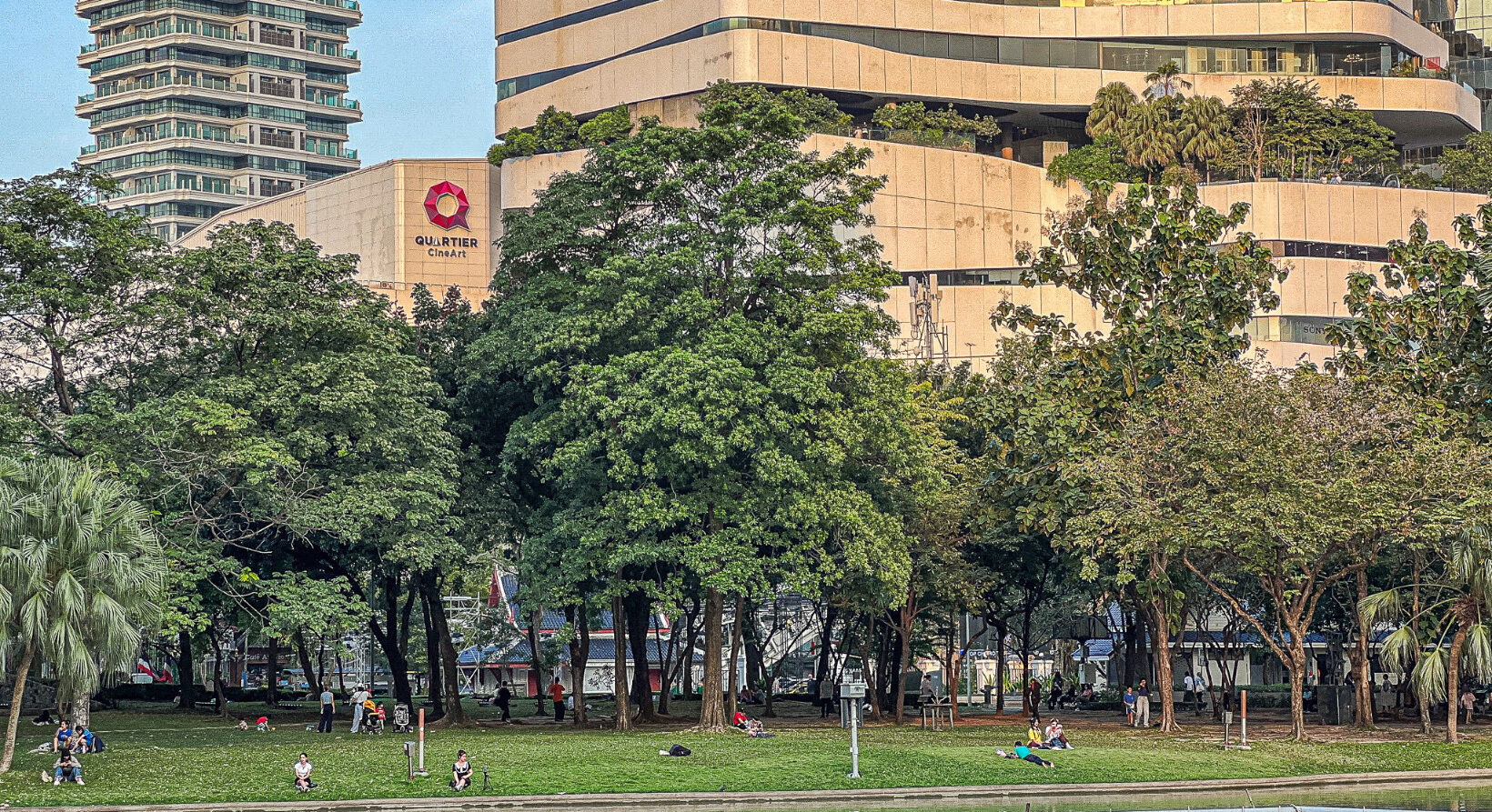 Trees and open lawn at Benjasiri Park Bangkok with Quartier CineArt in the background