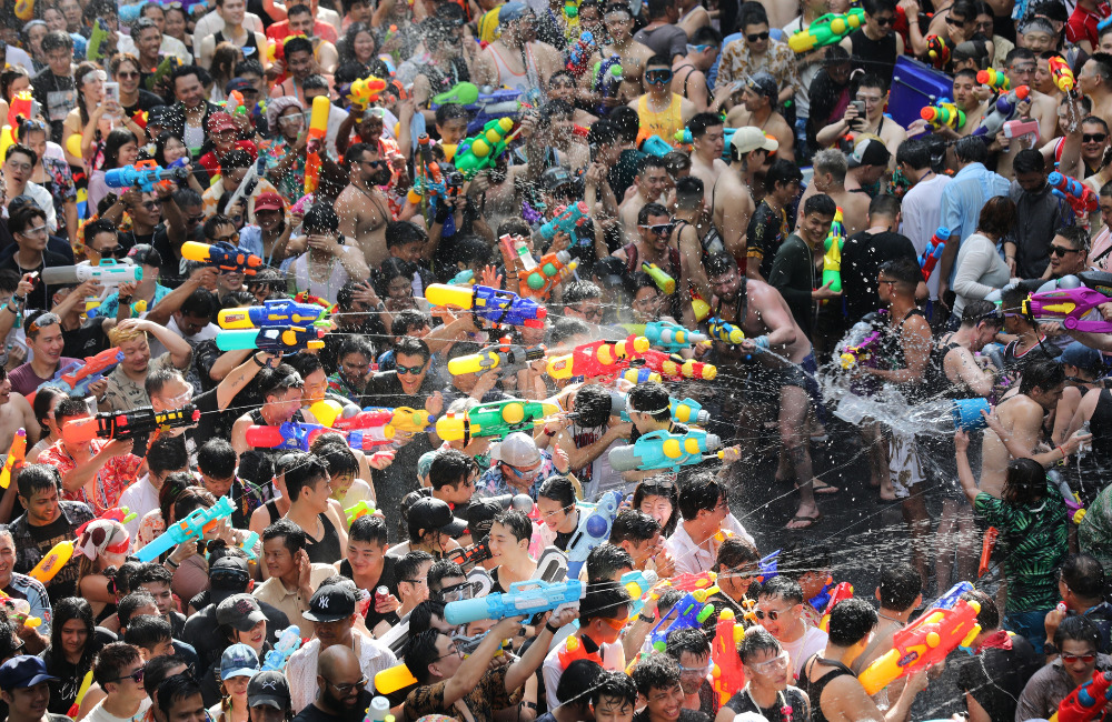 A high-energy crowd celebrating Songkran Festival 2026 in Bangkok, featuring people splashing water with colorful water guns during the Thai New Year festivities.