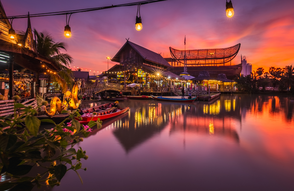 บรรยากาศตลาดน้ำ 4 ภาค พัทยายามเย็น แสงไฟสะท้อนผิวน้ำท่ามกลางท้องฟ้าสีม่วงส้มช่วงพระอาทิตย์ตก