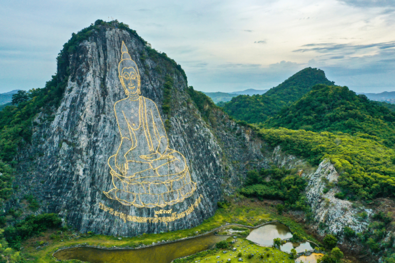 พระพุทธรูปแกะสลักบนหน้าผาเขาชีจรรย์ พัทยา รายล้อมด้วยธรรมชาติและภูเขาเขียวขจี