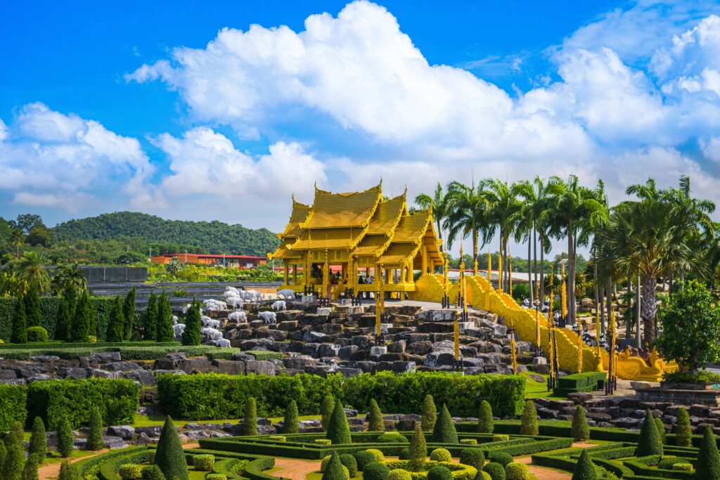 ศาลาทรงไทยสีทองในสวนนงนุช พัทยา รายล้อมด้วยสวนไม้ตัดแต่งสวยงามและต้นปาล์ม บรรยากาศสดใสท่ามกลางท้องฟ้าสีคราม