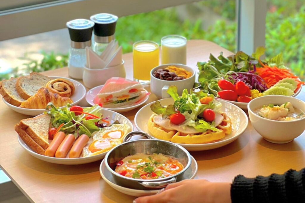 Hotel breakfast spread in Pattaya with fried eggs, sausages, toast, waffles, salad, cereal, soup, pastries, orange juice, and milk.